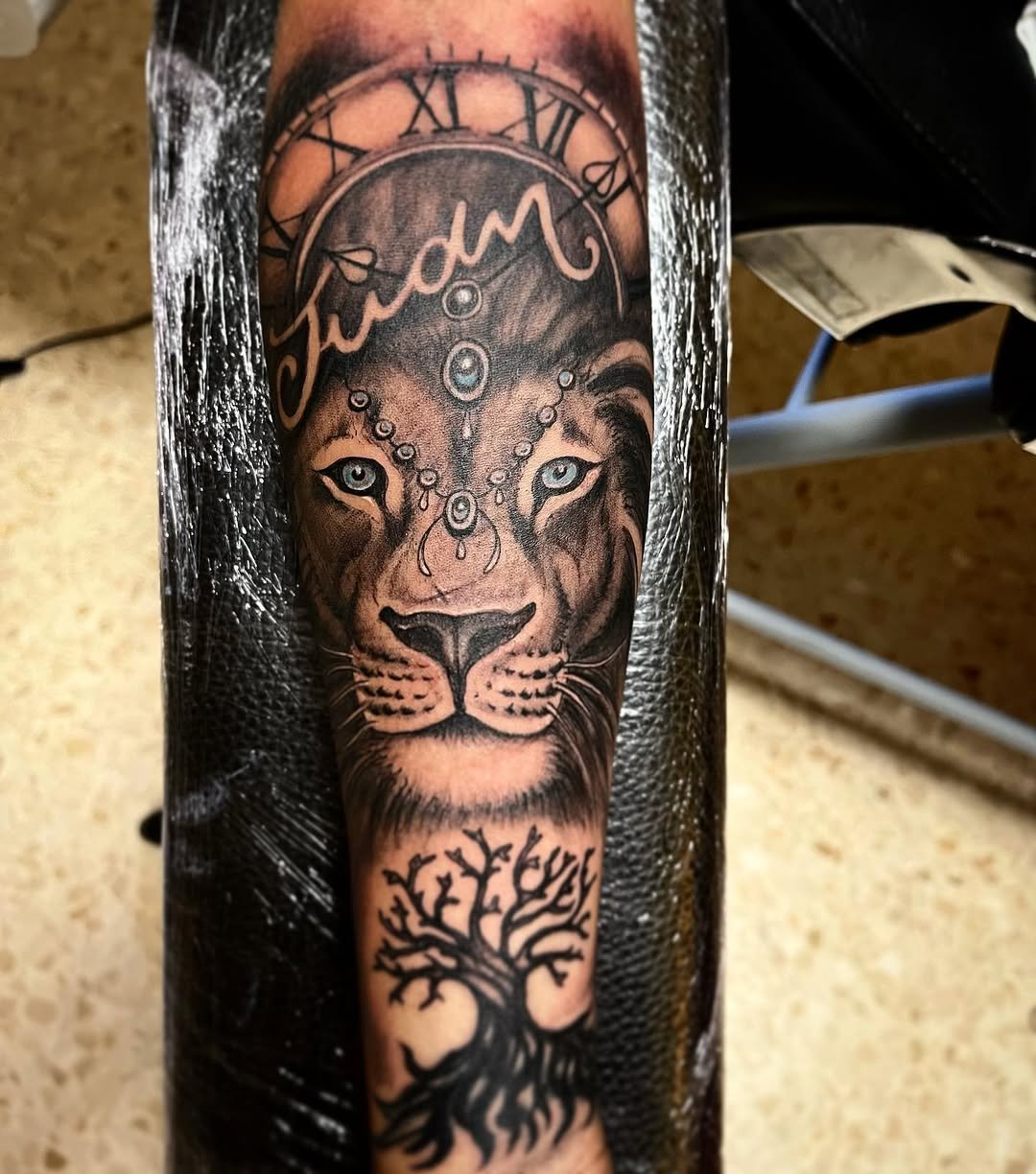 Tatuaje profesional en estudio MartinK Tattoo de un león, un reloj y un árbol