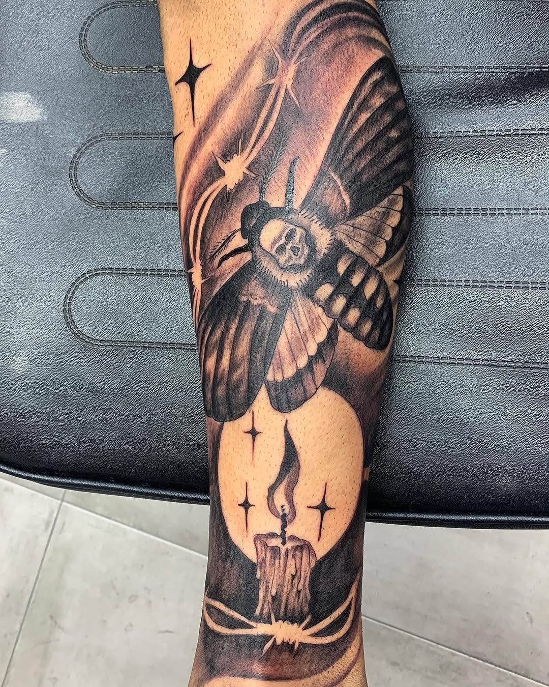 Tatuaje profesional en estudio MartinK Tattoo de una polilla con una vela